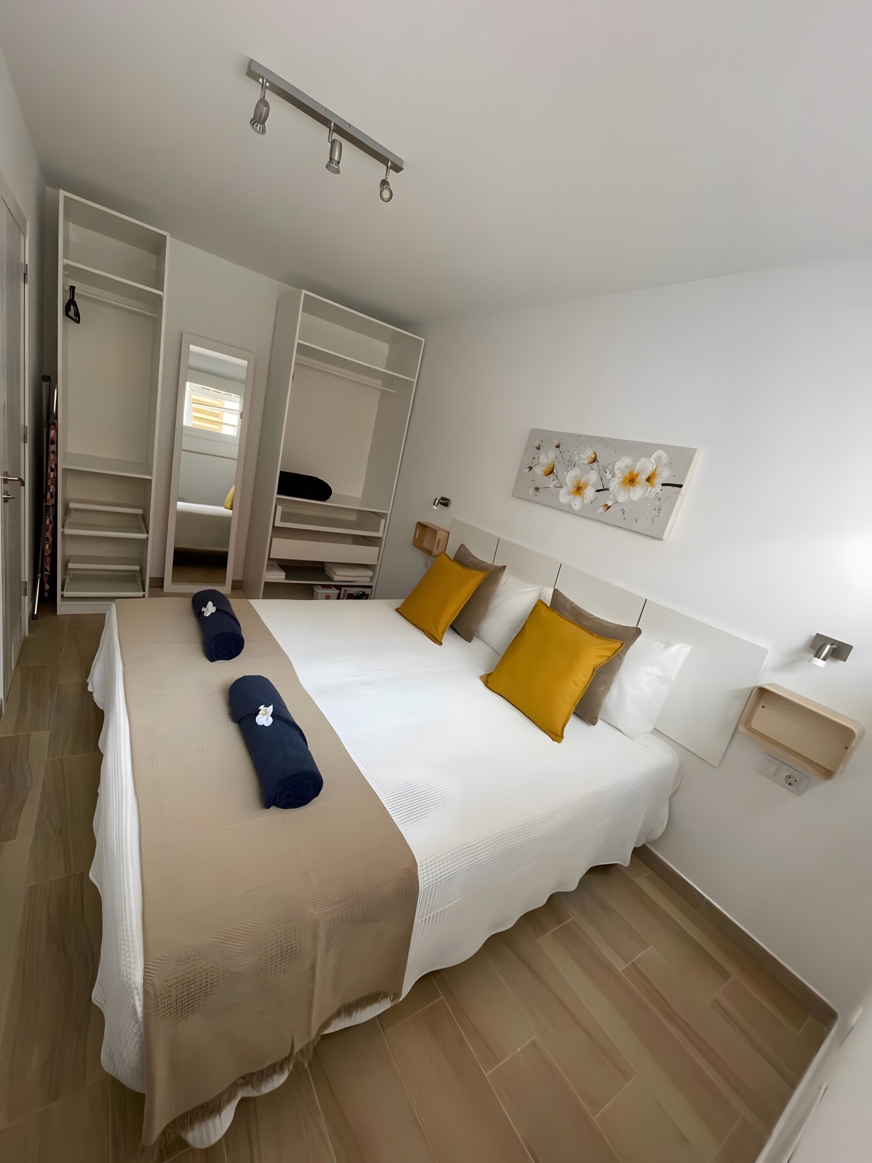 Hotellihuone, jossa on sänky, vaatekaappi, yöpöytä ja seinälle ripustettu taideteos.