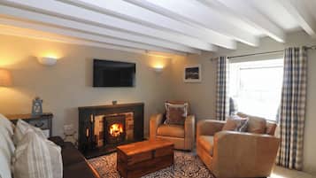 Una sala de estar con chimenea, un sofá, una silla, un televisor montado en la pared y un tapete estampado.