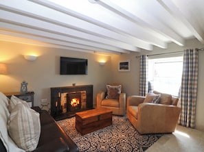 A living room with a fireplace, a sofa, a chair, a television mounted on the wall, and a patterned rug.