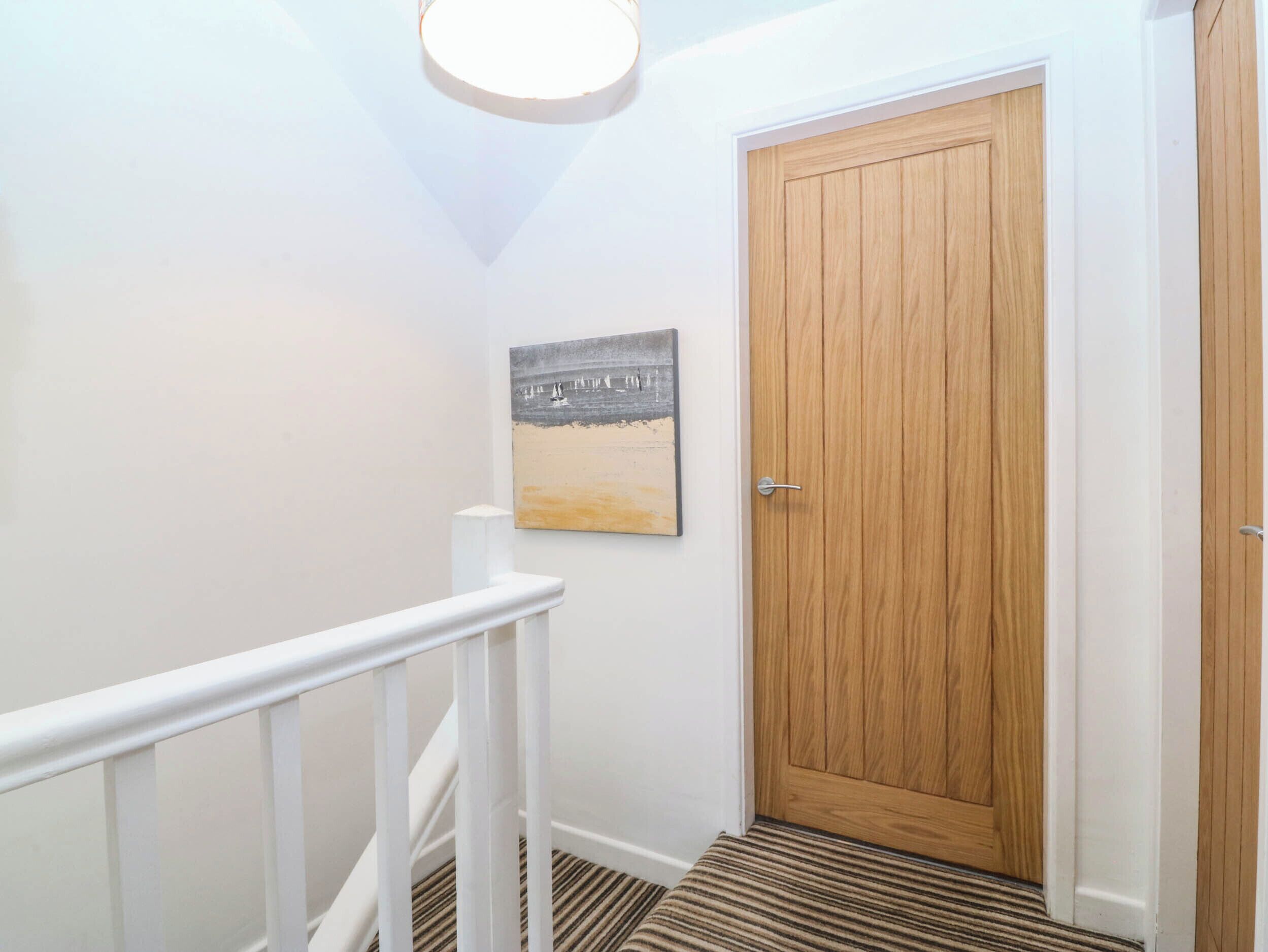A hallway with a wooden door, a white railing, and a striped carpet.