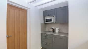 A compact kitchen with a microwave, toaster, and kettle on a countertop, a wooden door, and grey cabinets.