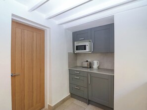 Cocina compacta con microondas, tostadora y hervidor sobre una encimera, una puerta de madera y armarios grises.