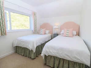 Un dormitorio con dos camas individuales, una ventana con cortinas, una mesita de noche con lámpara y vistas a zonas verdes.