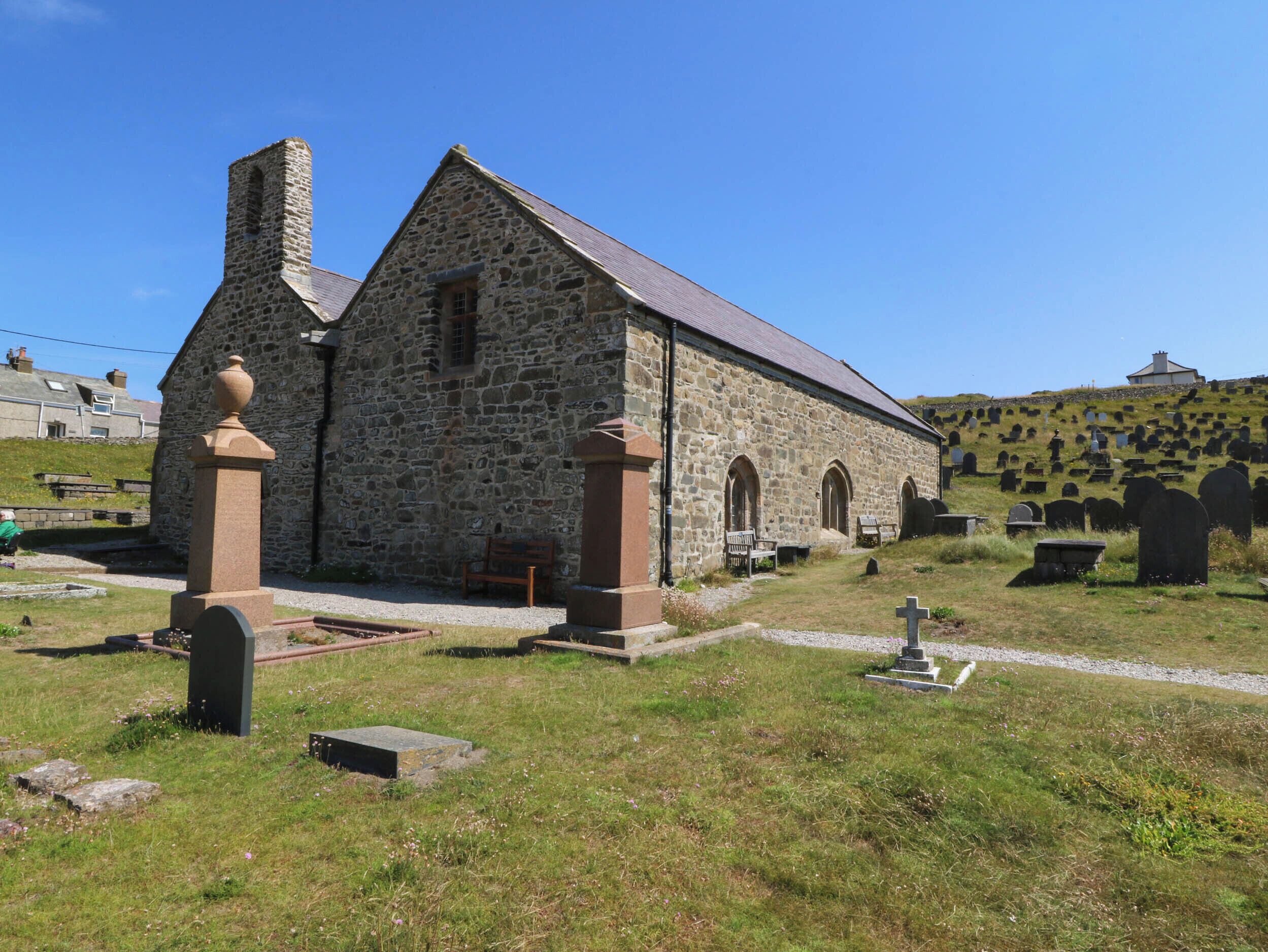Eine steinerne Kirche mit Glockenturm, Rundbogenfenstern und einem grasbewachsenen Friedhof im Hintergrund.