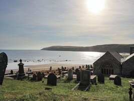 Un cementerio costero con lápidas de piedra, una iglesia y una playa al fondo.