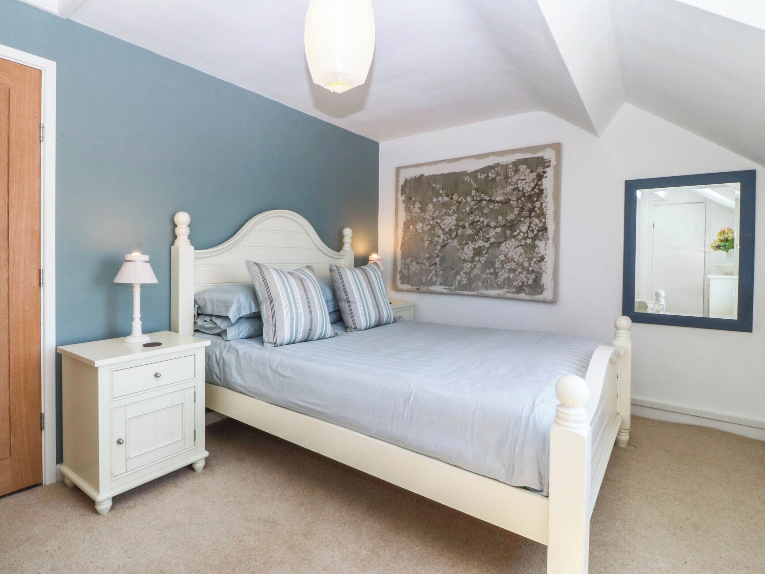 A bedroom with a bed, nightstand, and a wall-mounted mirror.