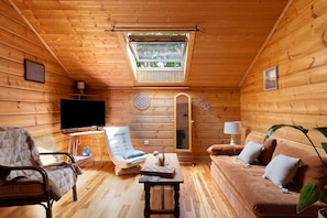 L’intérieur d’un chalet confortable, avec une télévision, un fauteuil rembourré, un canapé, une petite table et une lucarne.