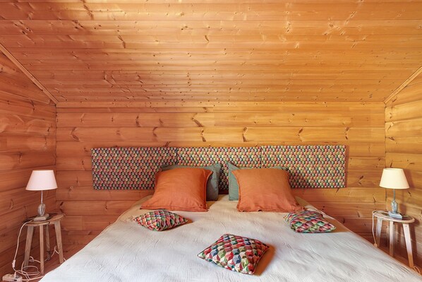 A wooden cabin room with a bed, two nightstands, and a patterned headboard.
