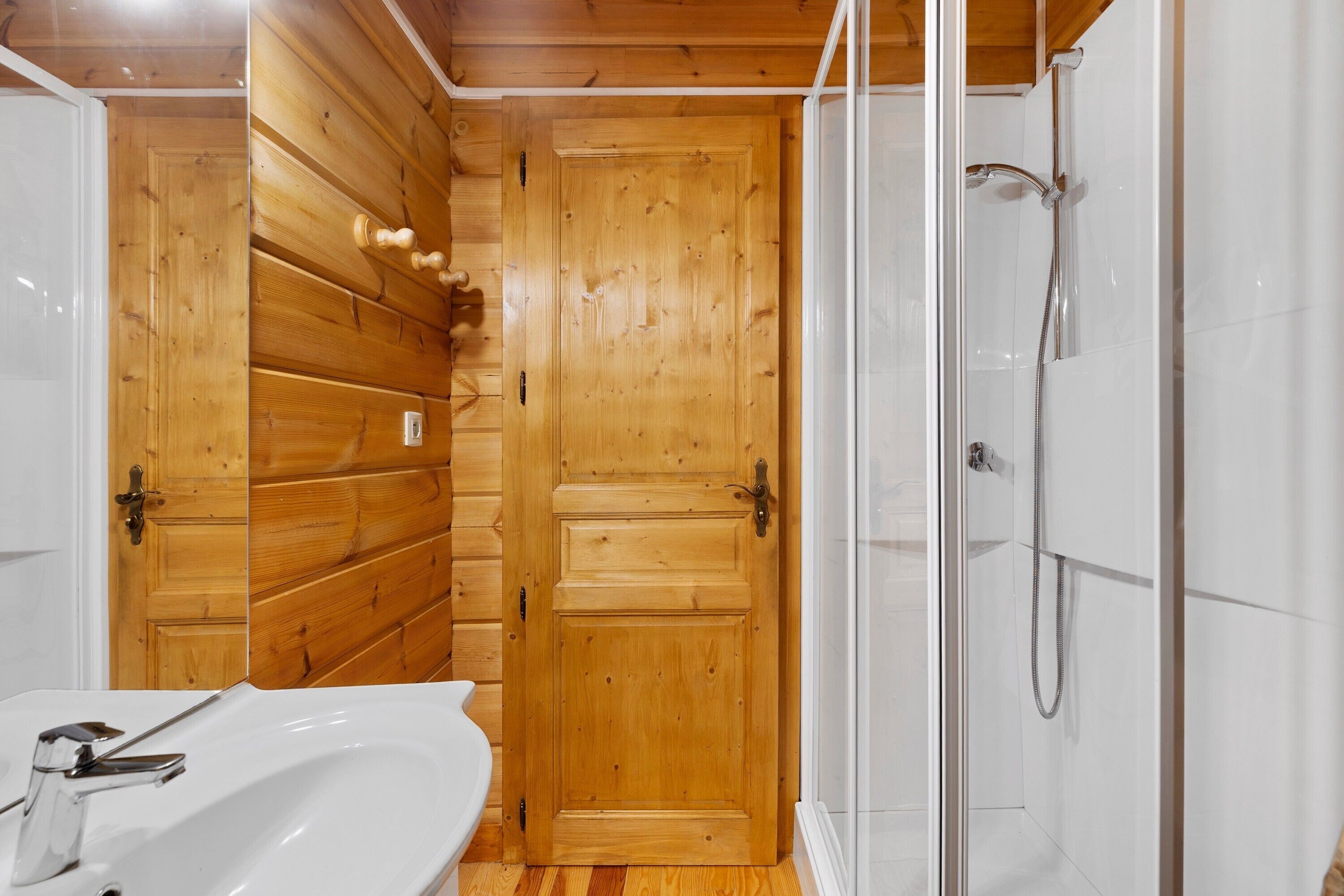 Een badkamer met houten lambrisering, een douche en een wastafel.