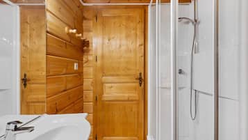 Een badkamer met houten lambrisering, een douche en een wastafel.