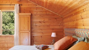 Un dormitorio de cabaña de madera con cama, almohadas, una mesita de noche y una ventana.