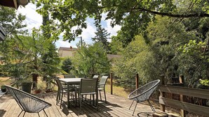 Un patio exterior con terraza de madera, una mesa con sillas y una hamaca.