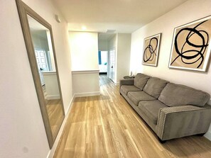 A hallway with a wooden floor, a grey sofa, and abstract art on the walls. - Premium 3BR 3.5BA | Patio & Garage | UTSW | DT (Dallas)