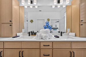 Une salle de bain moderne avec des meubles en bois, un grand miroir et une décoration à base d’orchidées bleues.
