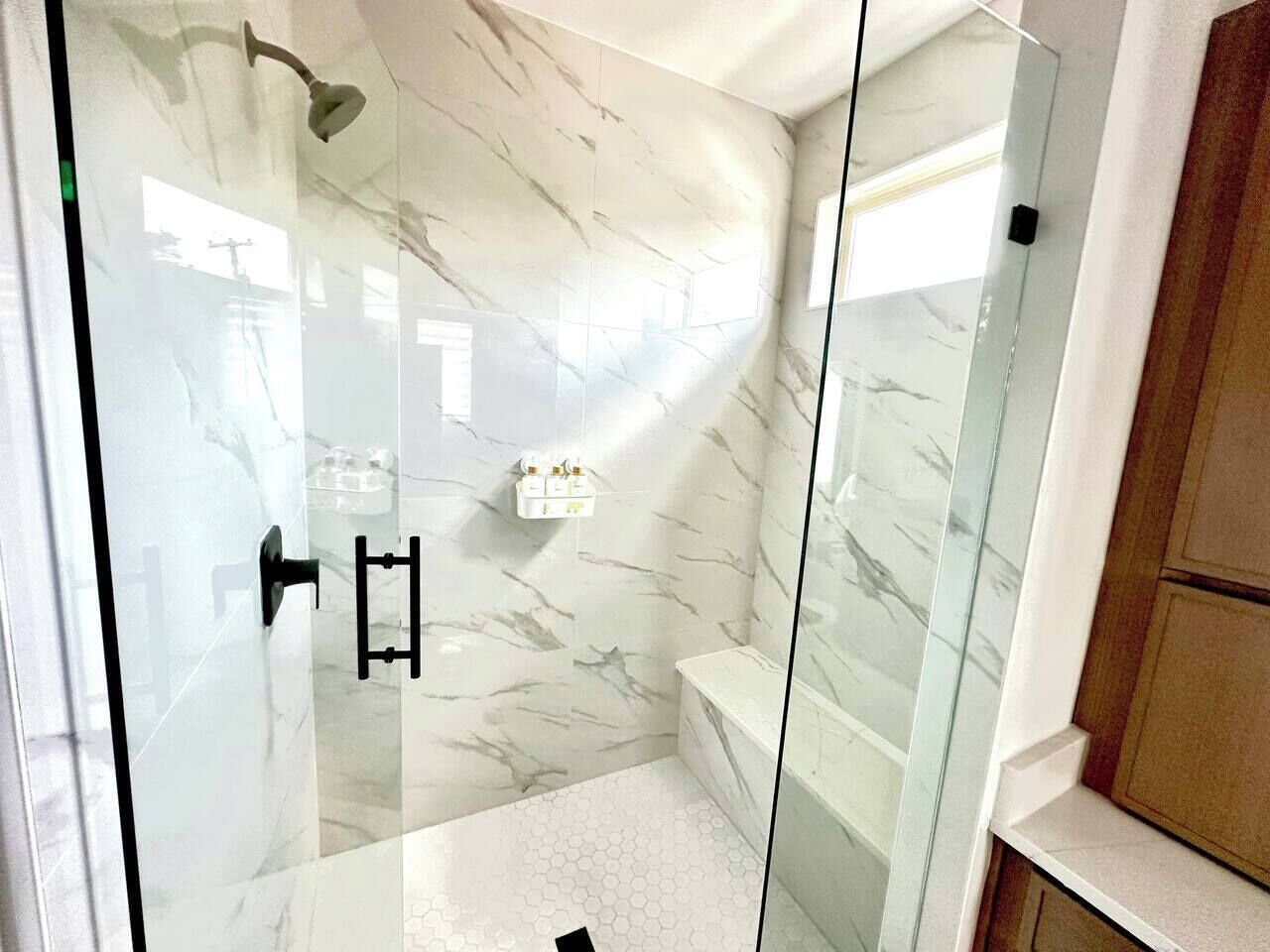 Een badkamer met een douchecabine van glas, marmeren wanden en een witte wastafel.