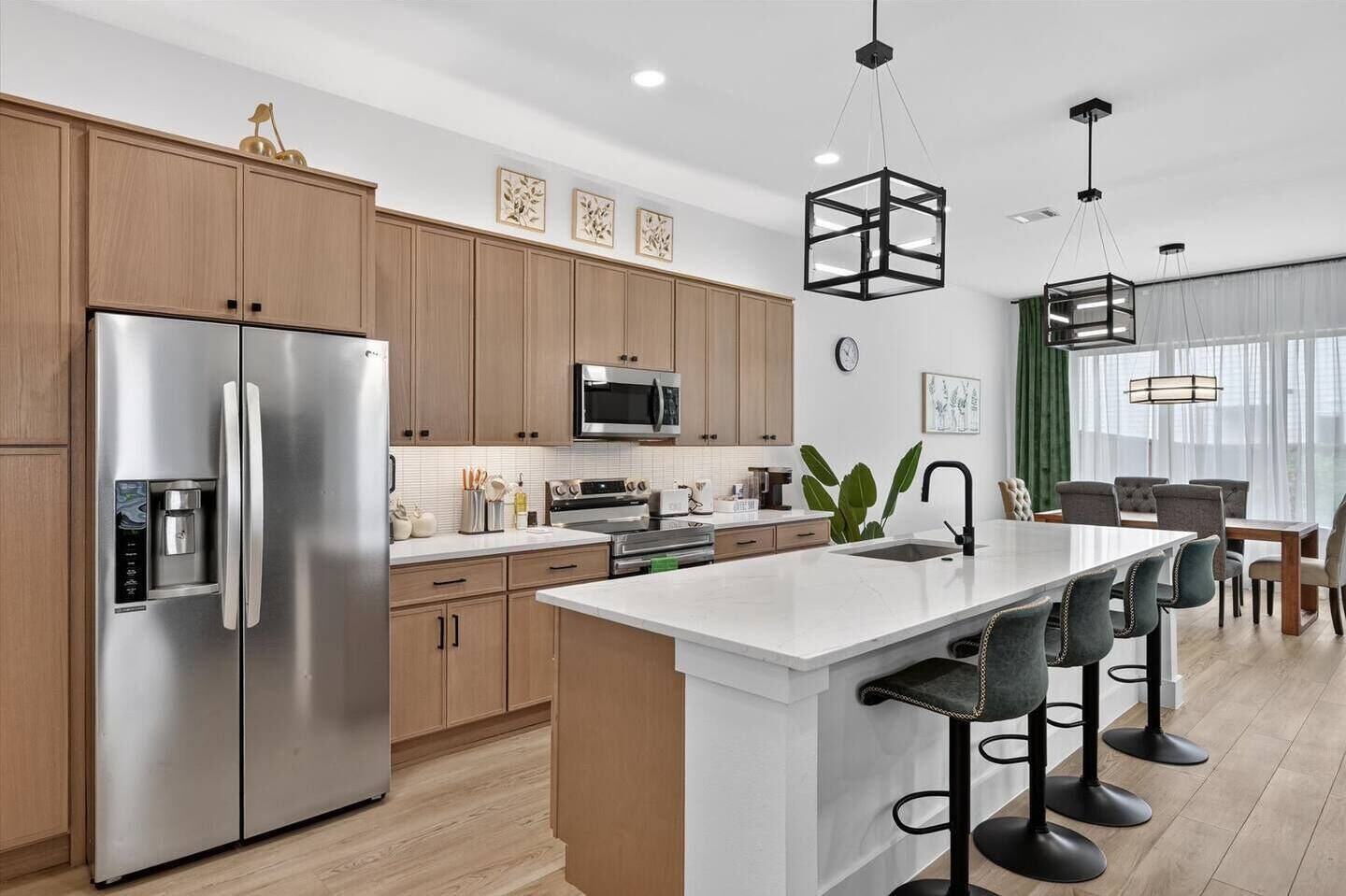 A modern kitchen with stainless steel appliances, wooden cabinets, a central island with bar stools, and pendant lighting.