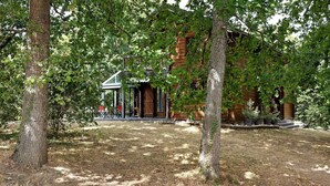 A rustic wooden building with a glass extension, surrounded by trees and a grassy area.