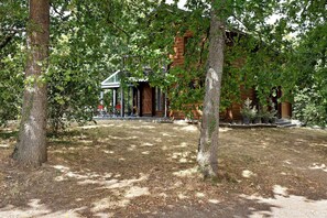 A rustic wooden building with a glass extension, surrounded by trees and a grassy area.