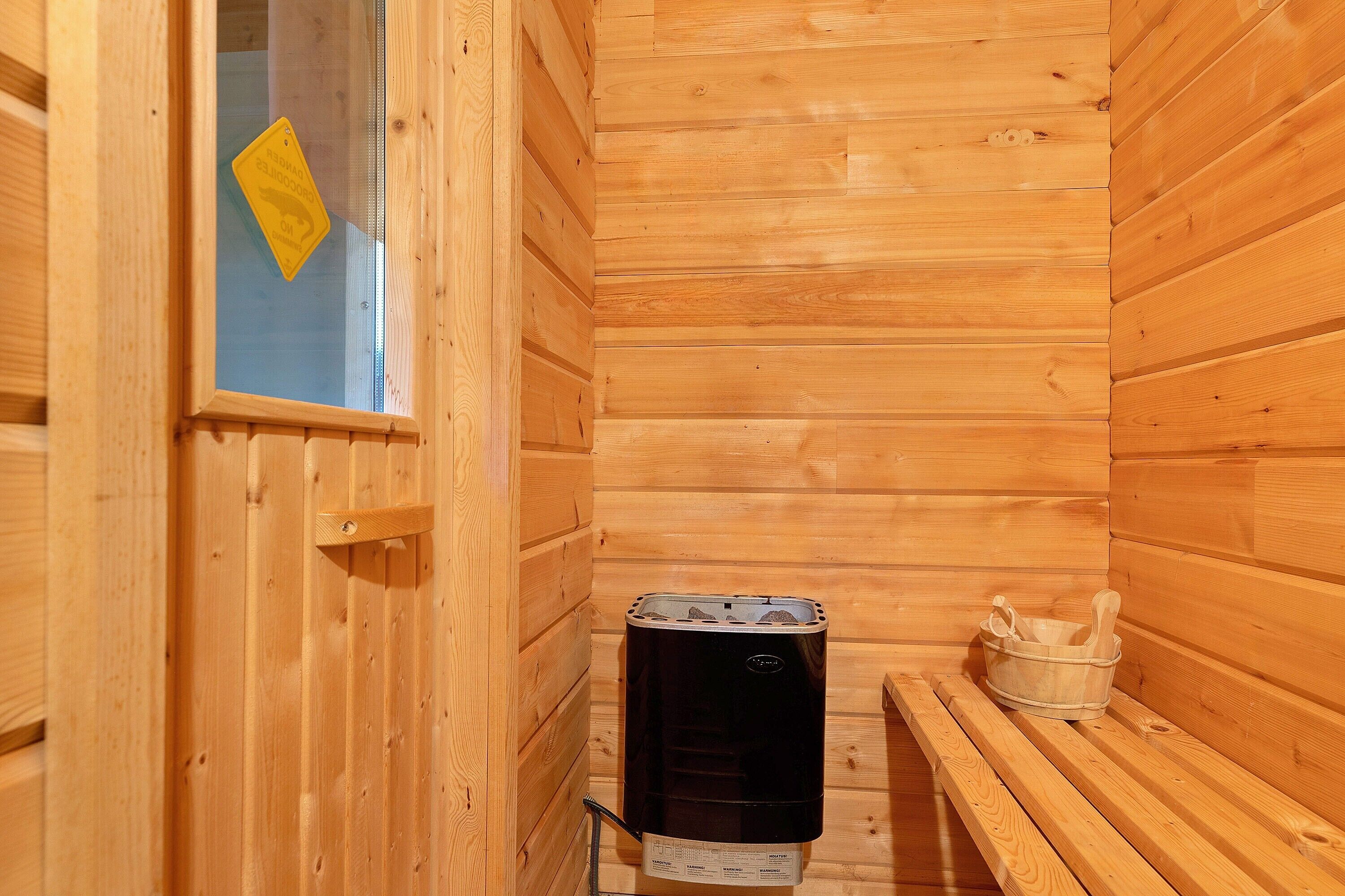 A wooden sauna room with a sauna heater, a bench, and a bucket.