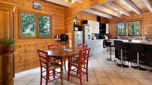 A wooden cabin interior with a dining area, kitchen, and large windows.