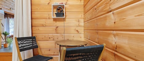 Un intérieur en bois avec deux chaises en osier et une petite table, un tableau encadré au mur et une plante en pot.