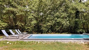 Piscina retangular com espreguiçadeiras e um deck pavimentado.