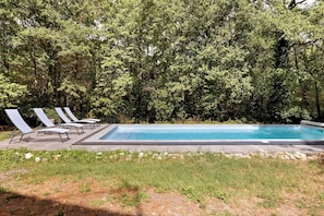 A rectangular swimming pool with a paved deck and lounge chairs.