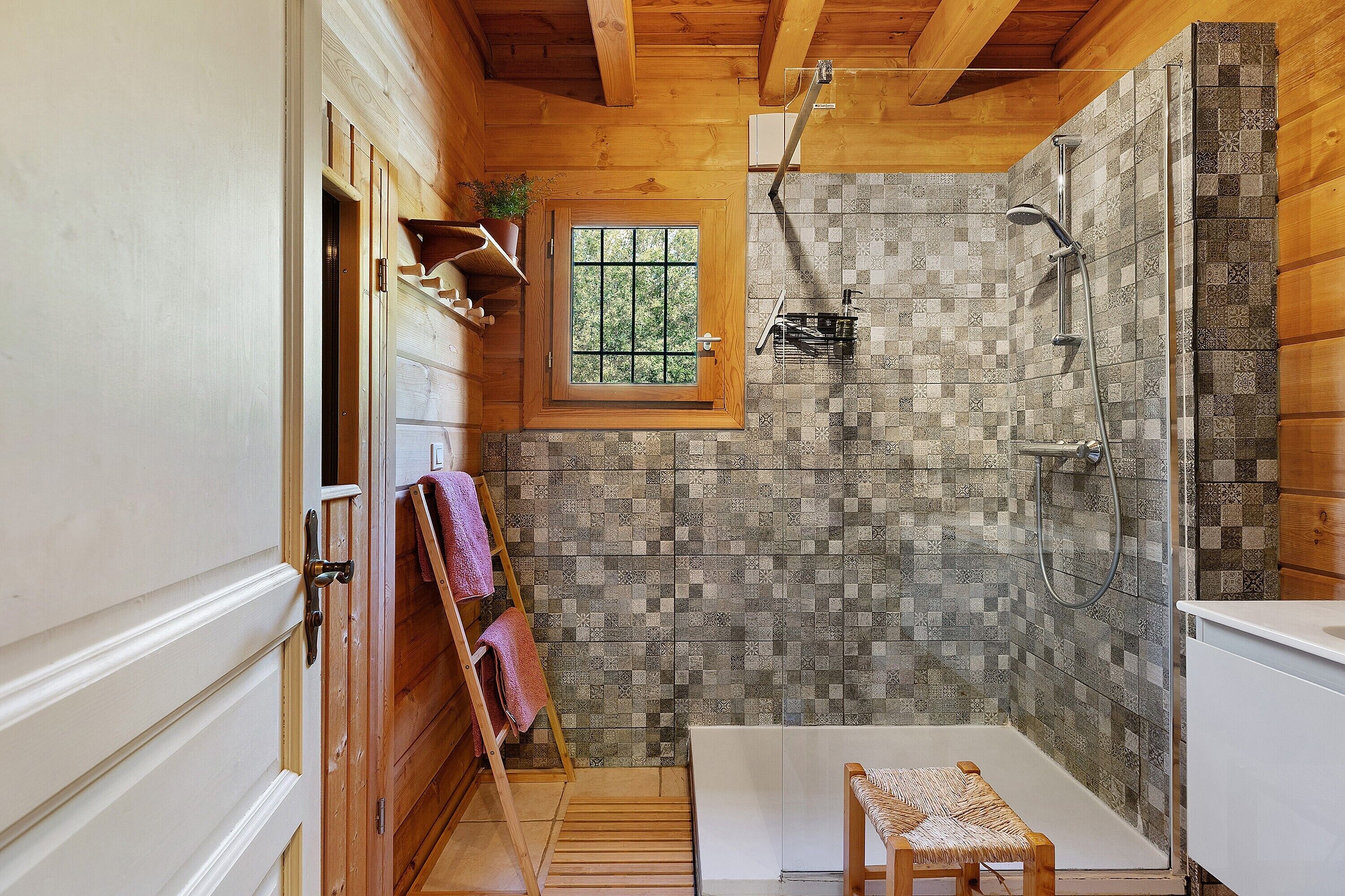 Un baño con ducha, una ventana, un perchero y un banco de madera.