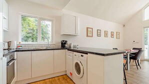 Eine moderne Küche mit integriertem Waschmaschine, eine Essecke mit Stühlen und ein Fenster mit Blick auf Bäume.
