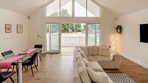 Ein geräumiges Zimmer mit hoher Decke, einem Glastisch, einem beigefarbenen Sofa und einem großen Fenster.