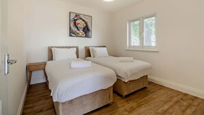 Ein Schlafzimmer mit zwei Betten, Holzboden, einem Bild an der Wand und einem Fenster mit Jalousien.
