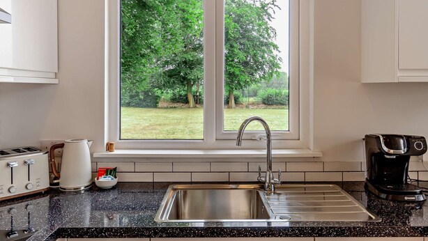 Eine Küche mit einer Edelstahl-Spüle, einem Fenster mit Blick auf Bäume, einem Wasserkocher und einer Kaffeemaschine.