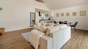 Ein modernes Wohnzimmer mit einer Couch, einem Essbereich mit Stühlen und einer Küche im Hintergrund.