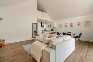 A modern living room with a sofa, a dining area with chairs, and a kitchen in the background. - Host & Stay | Robin Lodge (Burgh Castle)
