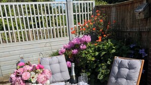 An outdoor patio with a round table, two chairs, a vase of flowers, a bottle, and a plate of olives. - Moss Retreat Sleeps 2, Balcony/garden/parking/pubs (Nantwich)