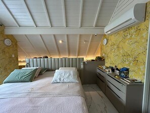 Ein Schlafzimmer mit einem Bett, Nachttischen, einer Kommode, einem Deckenventilator und einer Wandklimaanlage.