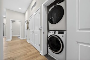 A laundry room with two stacked washers and dryers, white walls, and a wooden floor. - Modern Luxe • 2BR In Prime Philadelphia (Philadelphia)