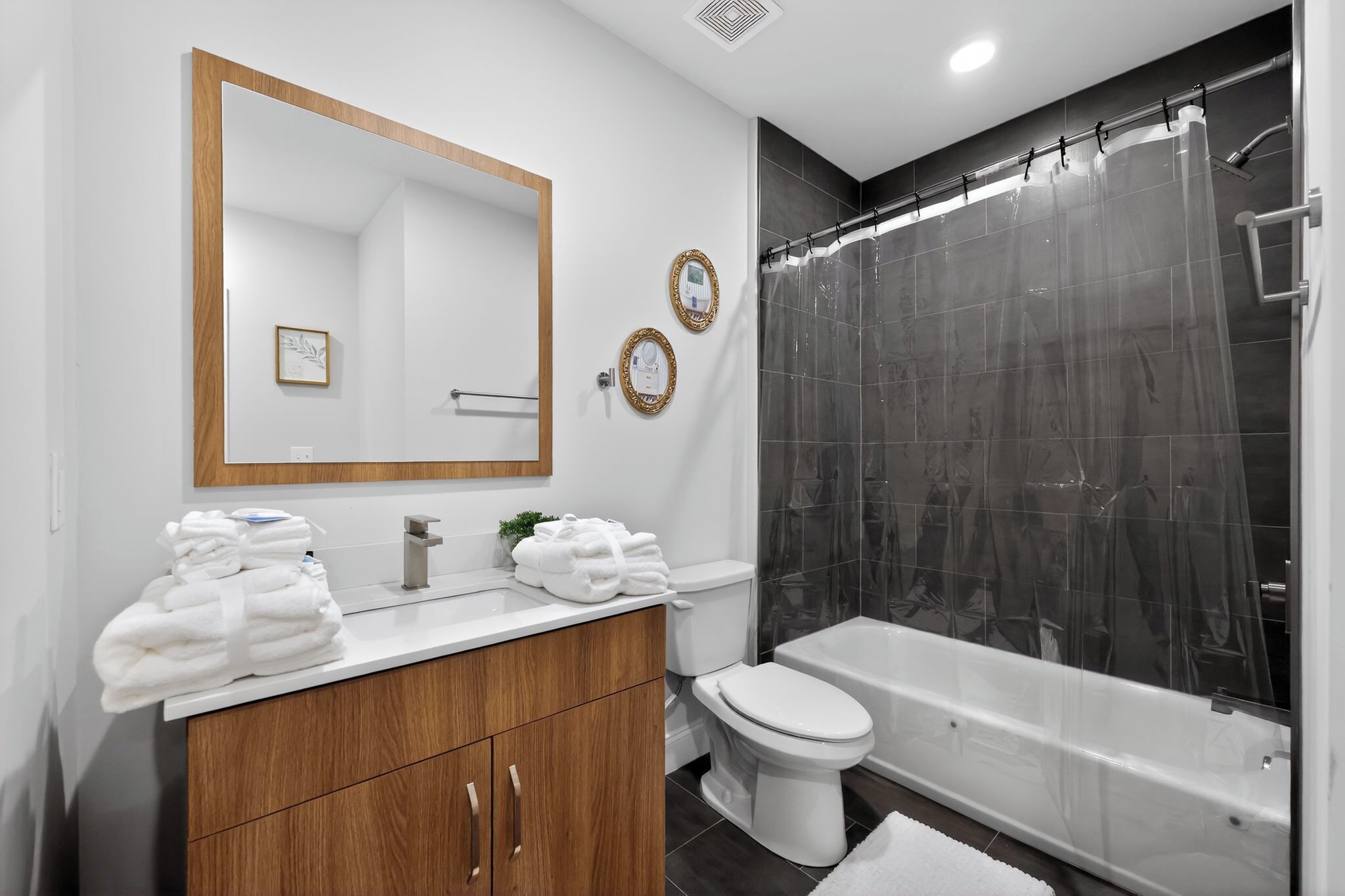Une salle de bain moderne avec un meuble-lavabo en bois, des toilettes blanches, une baignoire et un rideau de douche.