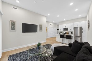 A modern living room with a black sofa, a glass coffee table, and a TV mounted on the wall. - Modern Luxe • 2BR In Prime Philadelphia (Philadelphia)
