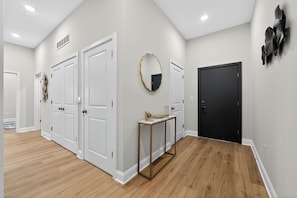 A hallway with white doors, a black door, and a small table with a mirror. - Modern Luxe • 2BR In Prime Philadelphia (Philadelphia)