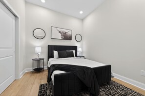 A modern bedroom with a black bed, white bedding, two bedside tables with lamps, a round mirror, and a framed picture on the wall. - Modern Luxe • 2BR In Prime Philadelphia (Philadelphia)