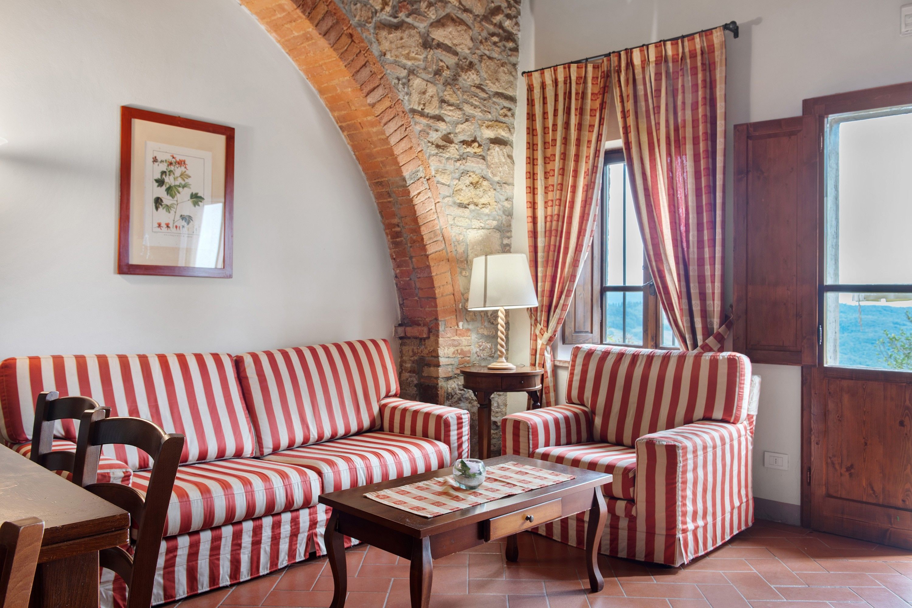 A room with a stone wall, a sofa, a chair, a table, and a window with curtains.
