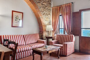 Una habitación con pared de piedra, un sofá, una silla, una mesa y una ventana con cortinas.