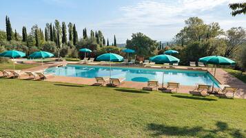 Ein rechteckiger Pool mit einer umlaufenden Liegefläche, ausgestattet mit mehreren Liegestühlen und Sonnenschirmen.