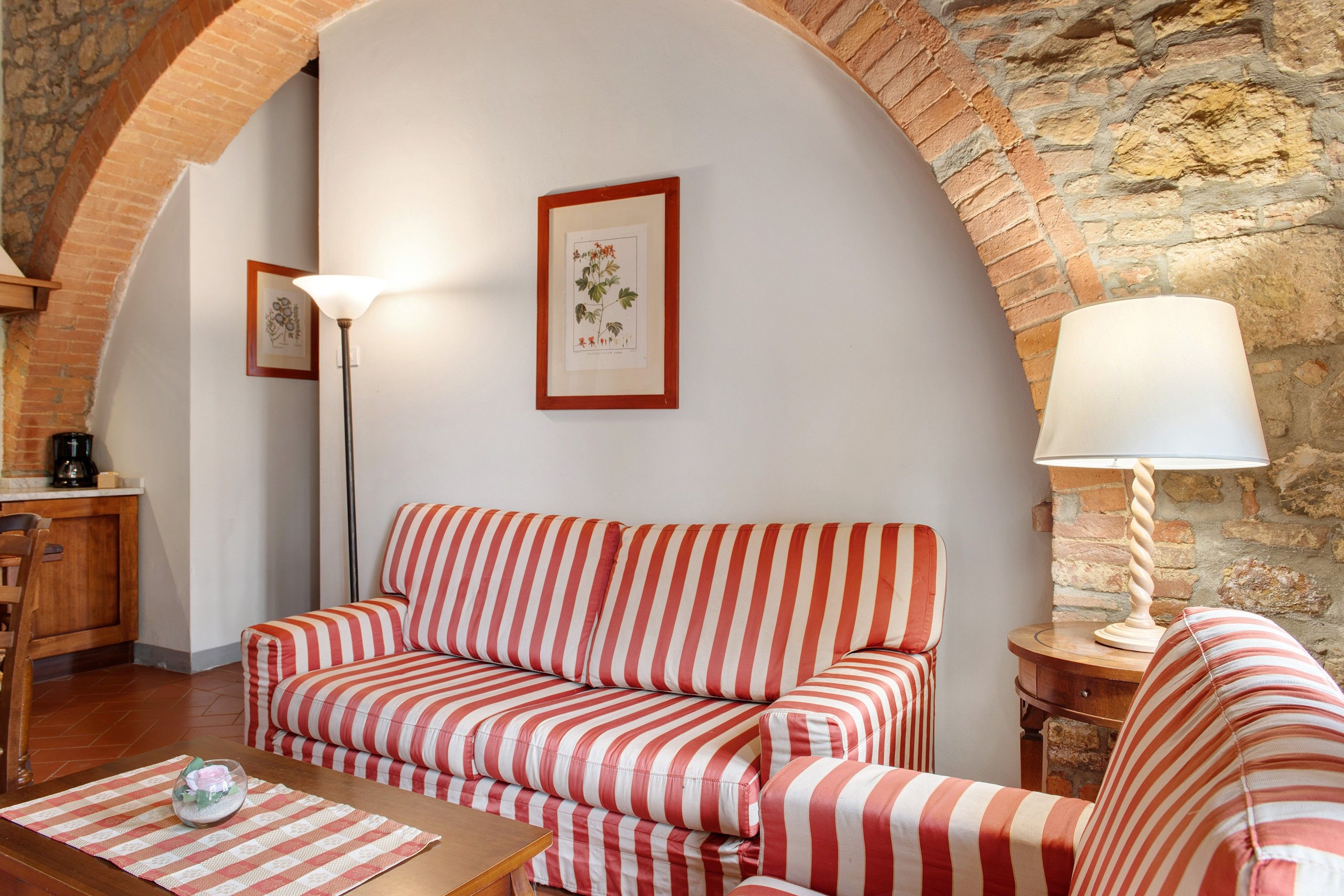 Una habitació acollidora amb un sofà a ratlles, una làmpada i reproduccions botàniques emmarcades a la paret.