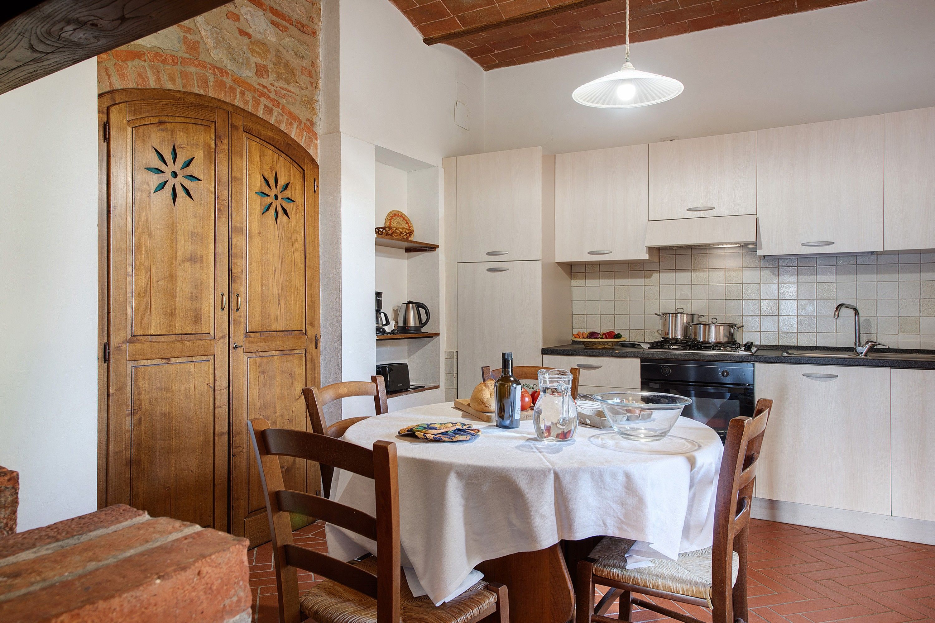 Una cocina con armarios blancos, una mesa de comedor con sillas y una pared de ladrillo.