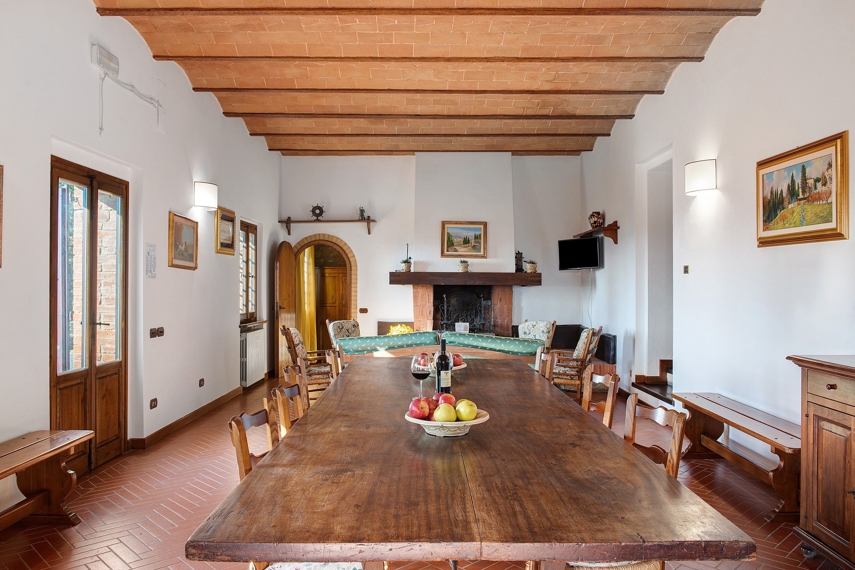A dining room with a long wooden table, chairs, a fireplace, and a television mounted on the wall.