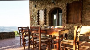 A rustic stone building with a wooden table and chairs, a view of the mountains, and a stone wall. - Caccia - Spacious Apartment with Views of the Tuscan Hills (Gambassi Terme)