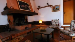 A cozy living room with a fireplace, floral-patterned furniture, and a wooden ceiling. - Caccia - Spacious Apartment with Views of the Tuscan Hills (Gambassi Terme)