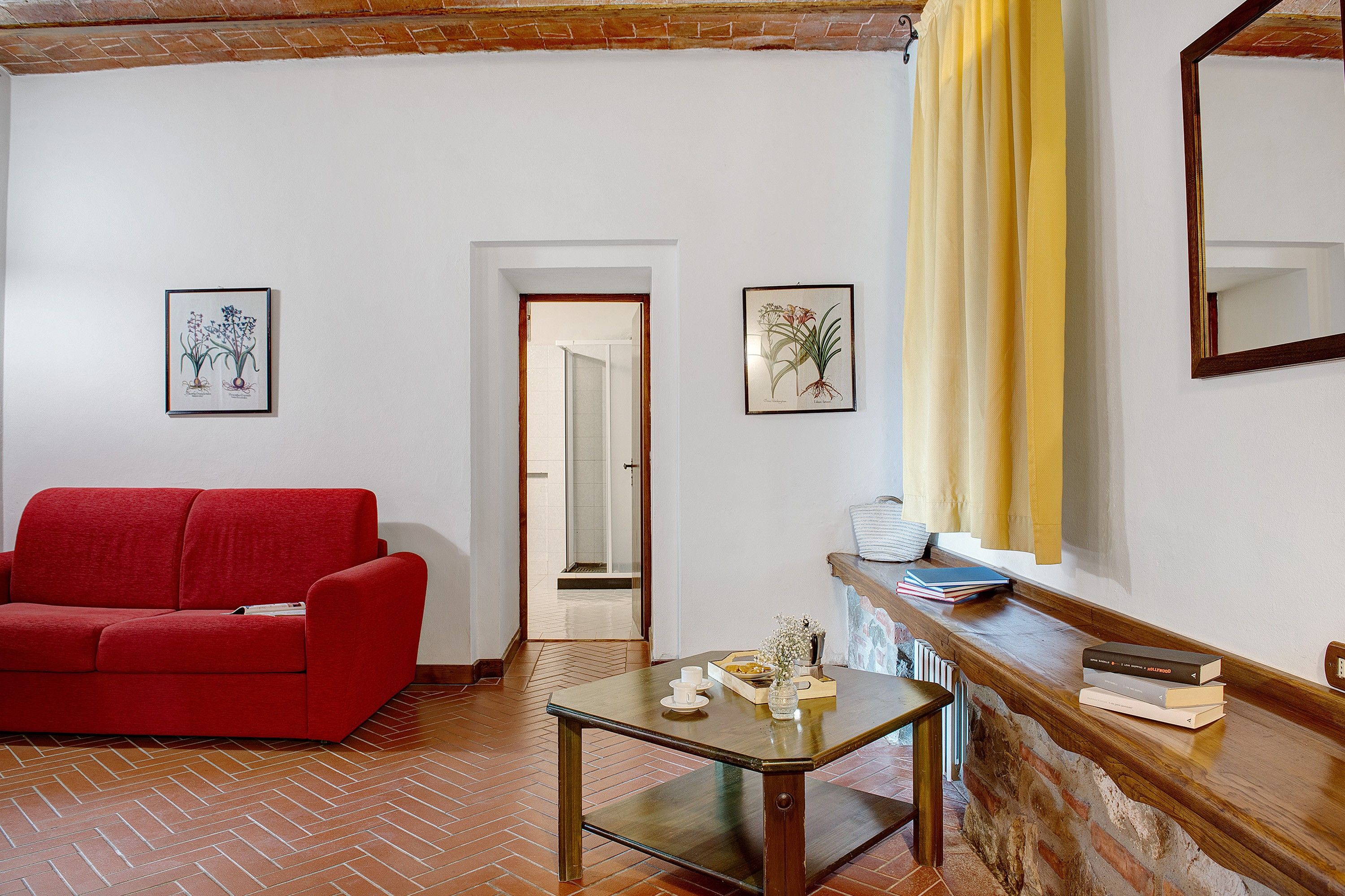 A room with a red sofa, a small table, and two framed botanical illustrations on the wall.